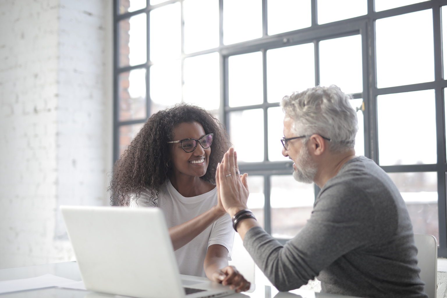 Happy male tutor giving high five to female student near computer in modern loft cafe
